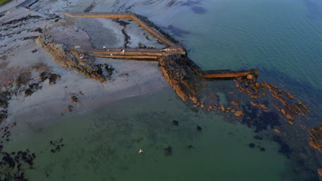 Dynamic aerial shot of Salthill coast showcasing its tidal pool bathed in golden sunset light. Galway