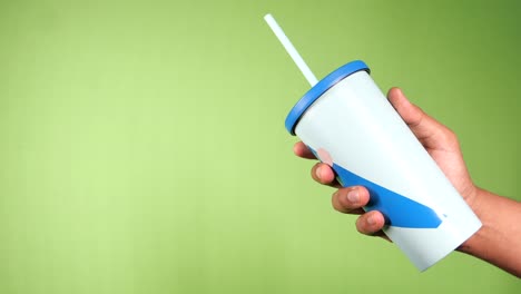 mano sosteniendo una taza de café ecológica reutilizable sobre un fondo verde
