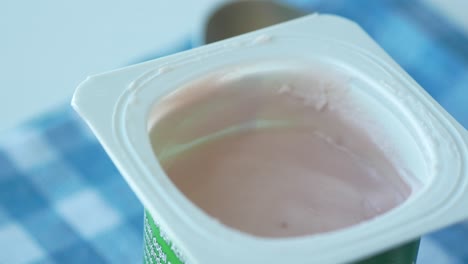 yogur fresco en un recipiente de plástico y una cuchara en la mesa