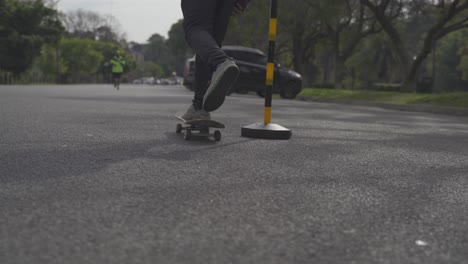 man rides skateboard between cones on street, follow behind