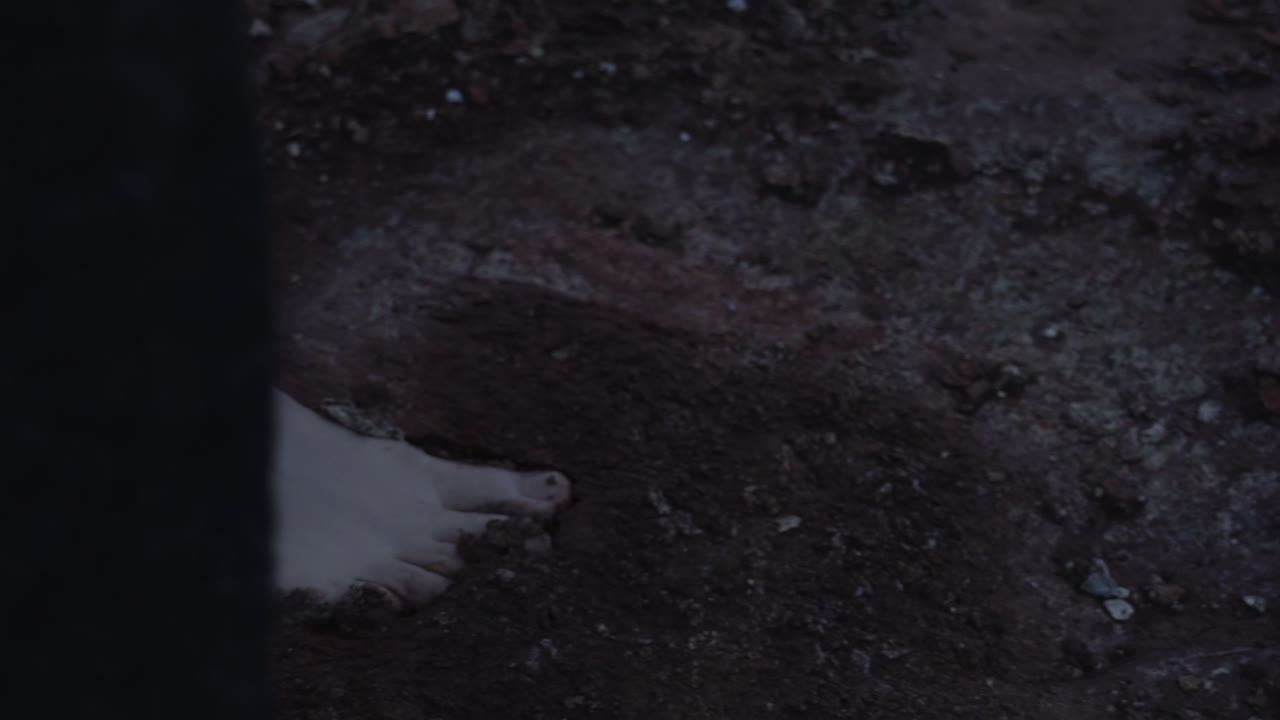 Close-up of woman's feet walking on wet volcanic terrain in Iceland, leaving footprints