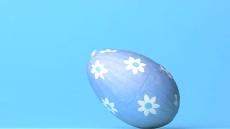 blue easter egg rolling across blue background