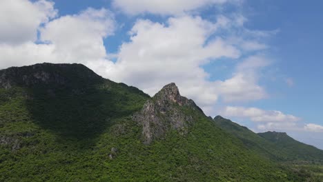 reverse aerial footage of this limestone mountains, a tower jutting out, clouds moving casting shadows during a lovely blue sky day