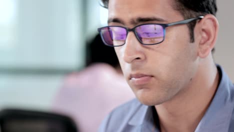 un apuesto joven empresario o empresario con gafas sonriendo en una configuración corporativa moderna.