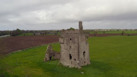 srah castle tower and grounds of old walls and holes on grassy field by farmland