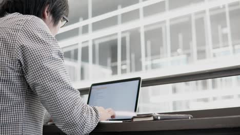 young asian business man using laptop computer in working space with smartphone and notebook on wooden desk. male hand typing on laptop keyboard. freelance lifestyle in digital age concept.