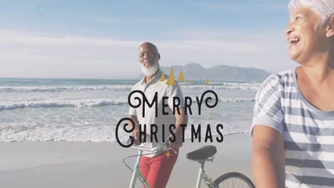 animation of merry christmas text over happy diverse senior couple with bikes on sunny beach