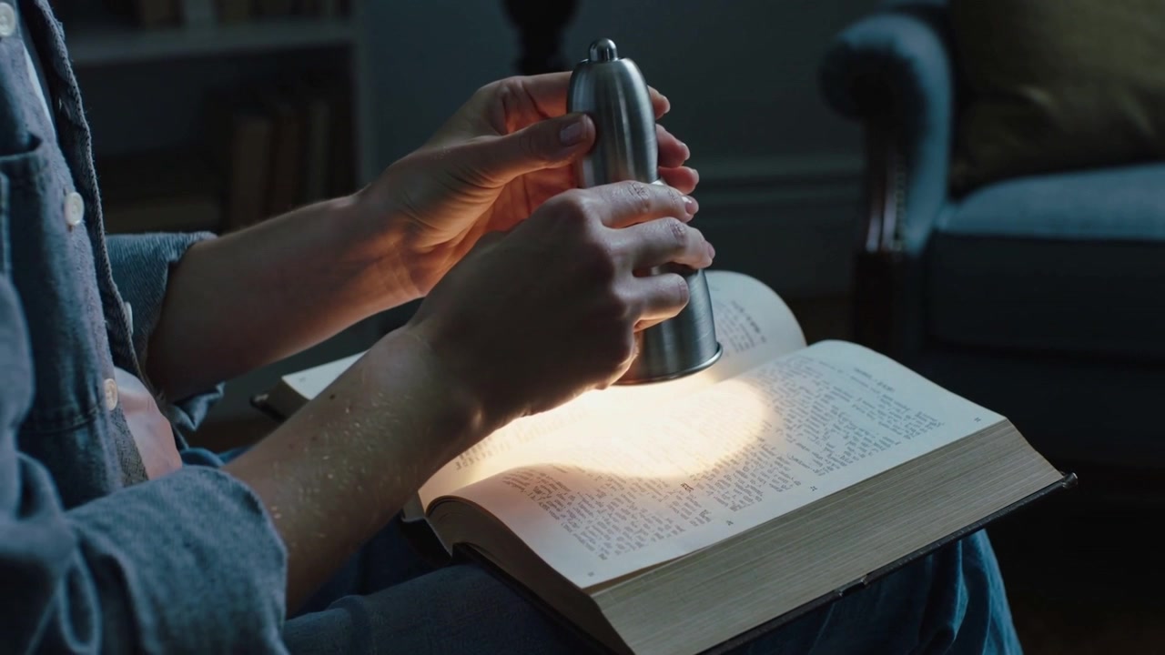Posizionando la lampada, lettore in camicia di jeans che inclina una lampada di metallo per centrare la luce sul libro in grembo