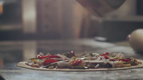 anonymous chef seasoning pizza with aromatic herbs