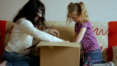 familia, mamá e hija abre el paquete de la tienda en línea. mujer joven mira en la caja, se sorprende y está feliz de recibir una sorpresa. chica abrió una caja con un regalo. cámara lenta.
