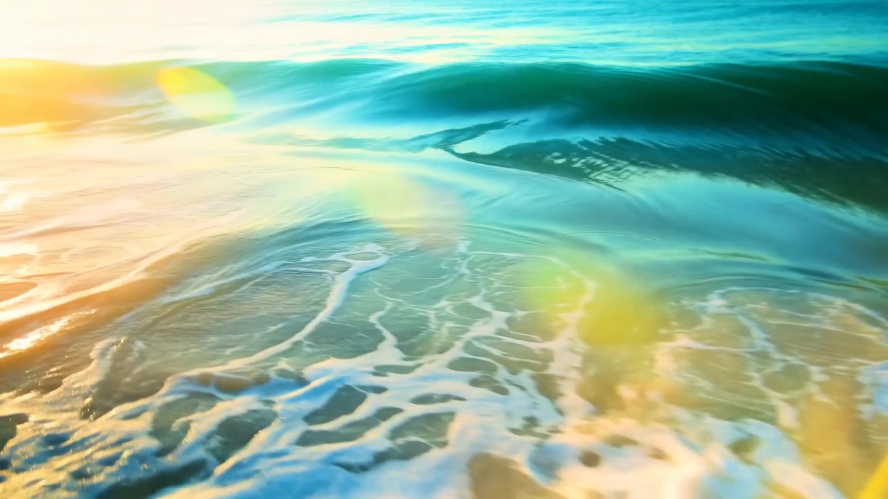 Vista ravvicinata dell'oceano che mostra le onde che si infrangono su una riva poco profonda con densa schiuma bianca in primo piano, una cresta turchese traslucida che si alza a metà campo, e una calda luce solare radente che crea riflessi scintillanti.