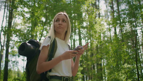 a traveler in the forest with a backpack walks along the path and looks at the mobile phone screen