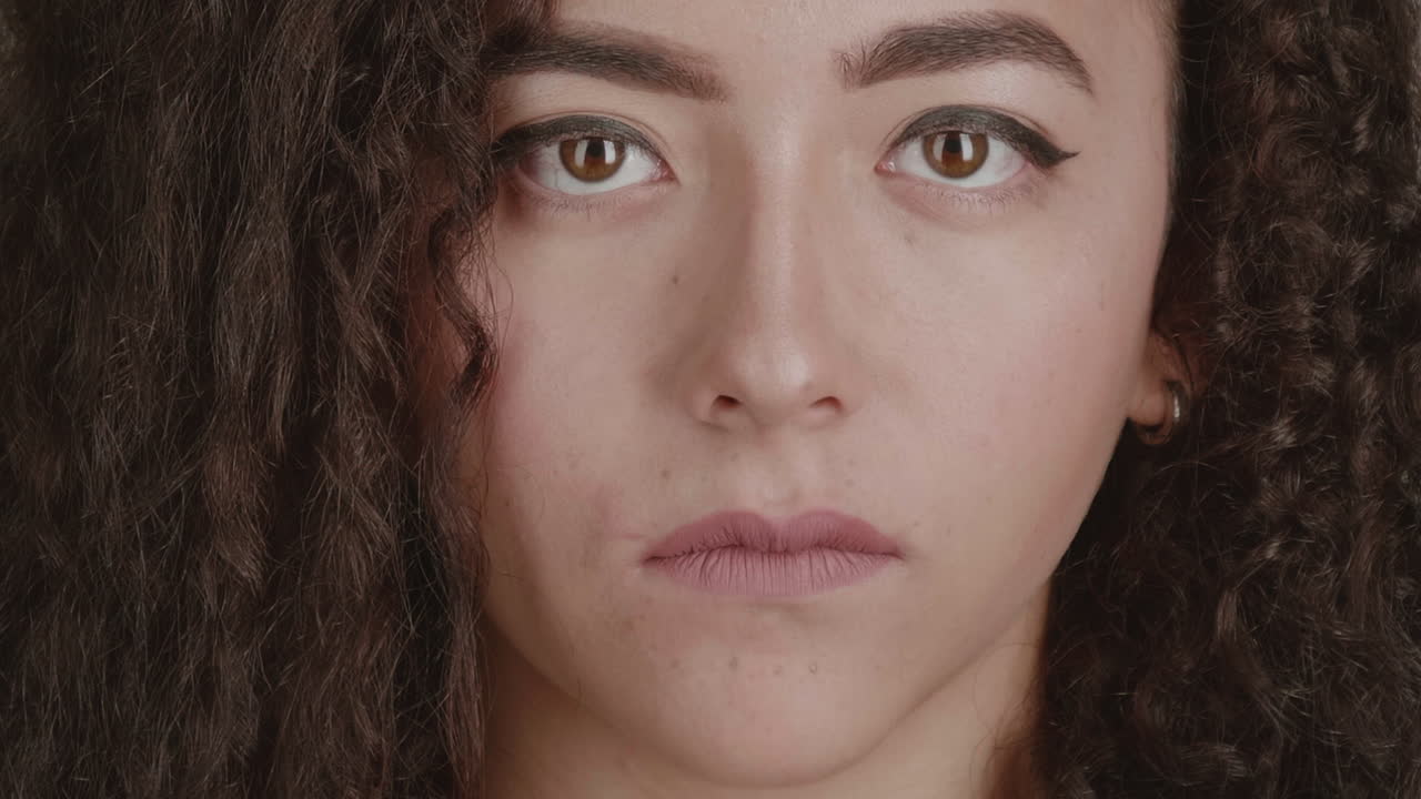 Close-up beauty portrait of a young woman with curly brown hair giving a slight smirk to the camera