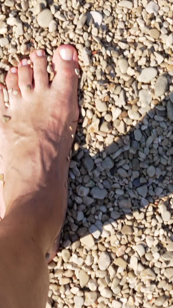 Piede che calpesta la spiaggia di ciottoli ed entra in acque poco profonde e limpide
