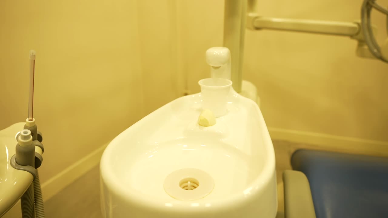 Dentist spittoon equipment with small plastic cup in dental clinic, next to some tools. Pull out shot, slow motion