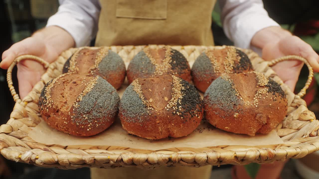 The baker holds in hands a of fresh bread with black poppy garnish on top close-up. Artisan bread is making by skill bakers using natural and high-quality ingredients. Food with health and flavour benefits.