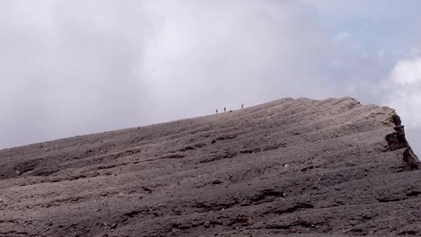 People in the distance walking up the crest of volcano to the summit and crater on a tough multi-day hike and climb adventure on remote tropical island of Bougainville, Papua New Guinea