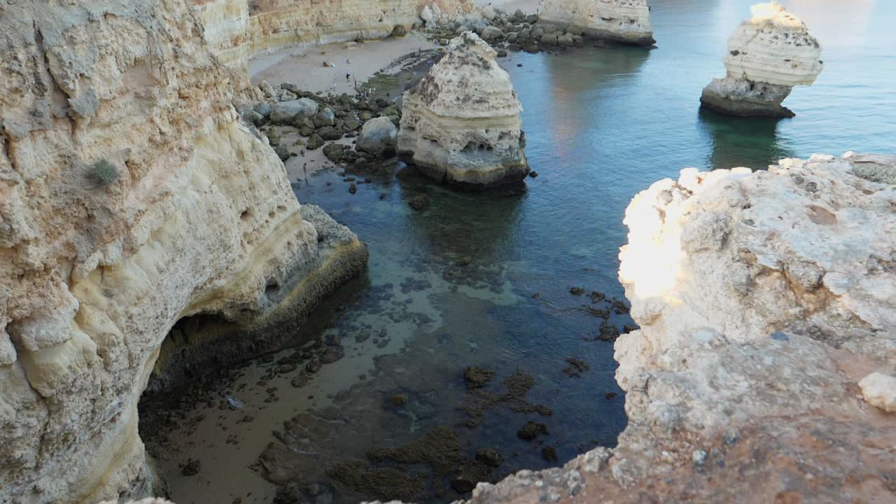 Tilting up shot, Scenic view of Rock Tunnels beach in Algarve, Portugal, people walking on the coastline in the background