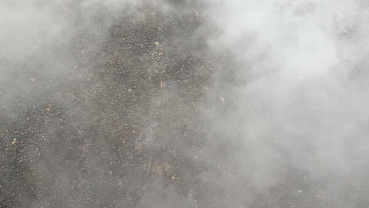 Dense white smoke billows upward from dark ground, natural daylight, static camera, outdoor environment