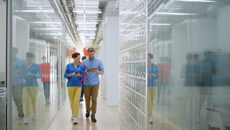 Man-and-woman-talking-in-office.-Colleagues-walking-with-digital-devices-indoors