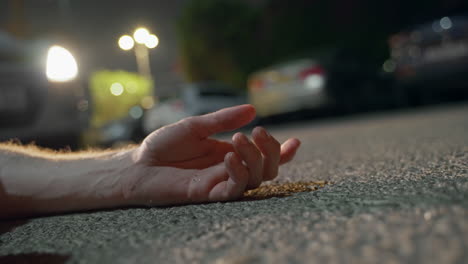 la mano del hombre yace inmóvil, iluminada por las luces intermitentes de un coche de policía.