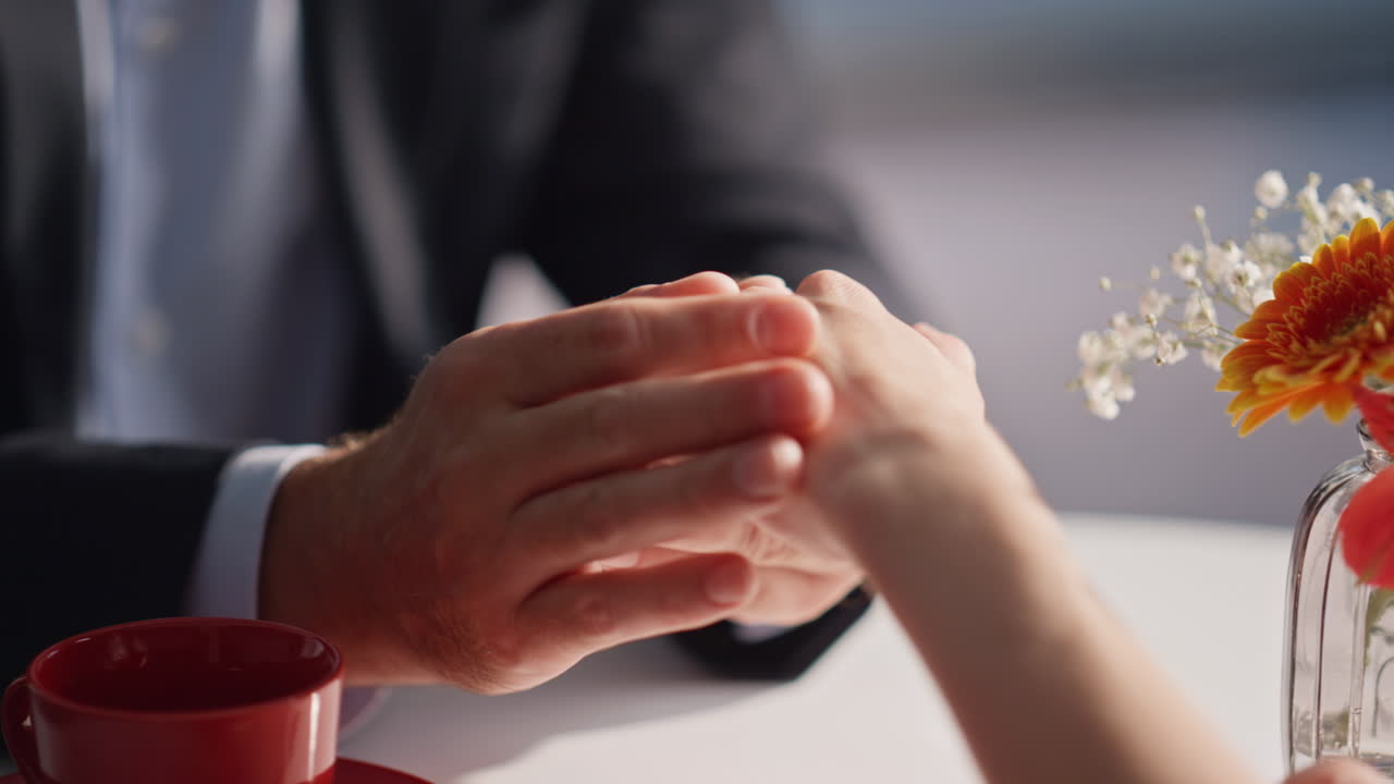Lovers hands holding gently at cafe table closeup. Unknown romantic couple