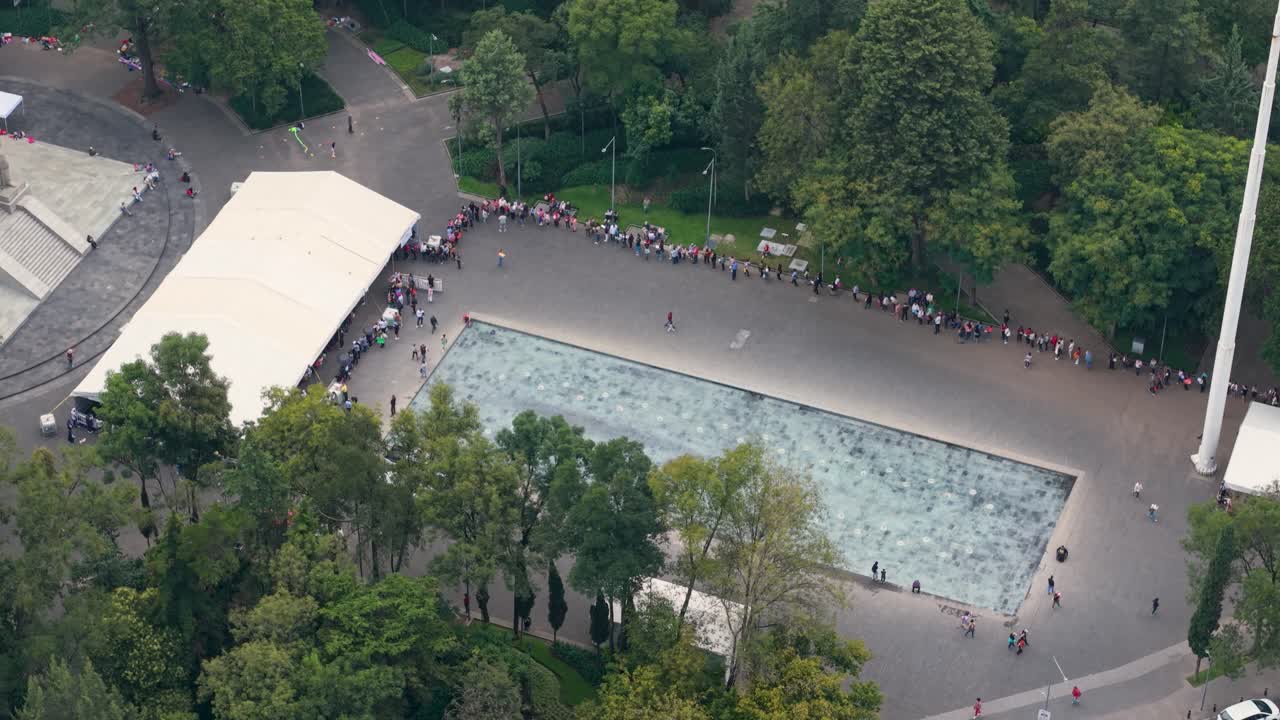 Drone view of crowds forming queues around water mirror in Mexico City park