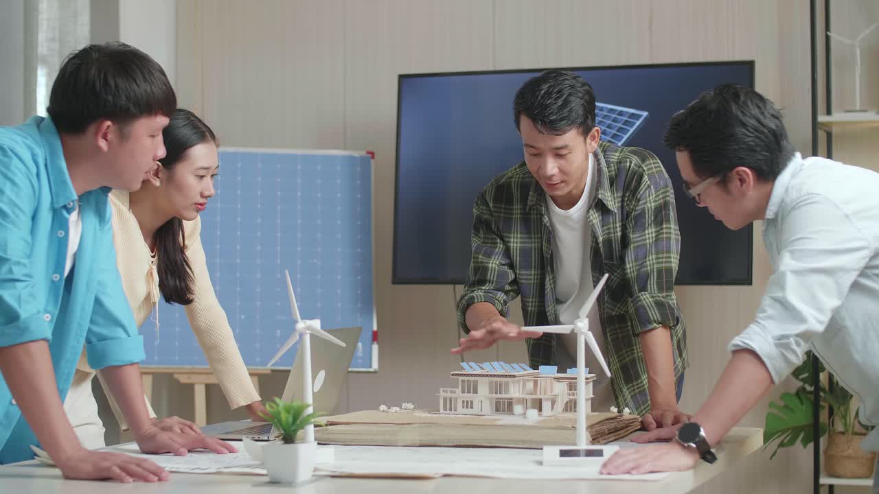 아시아 엔지니어 그룹이 사무실에서 태양 전지판을 가진 작은 집의 모델에 대해 회의를 하고 있습니다.