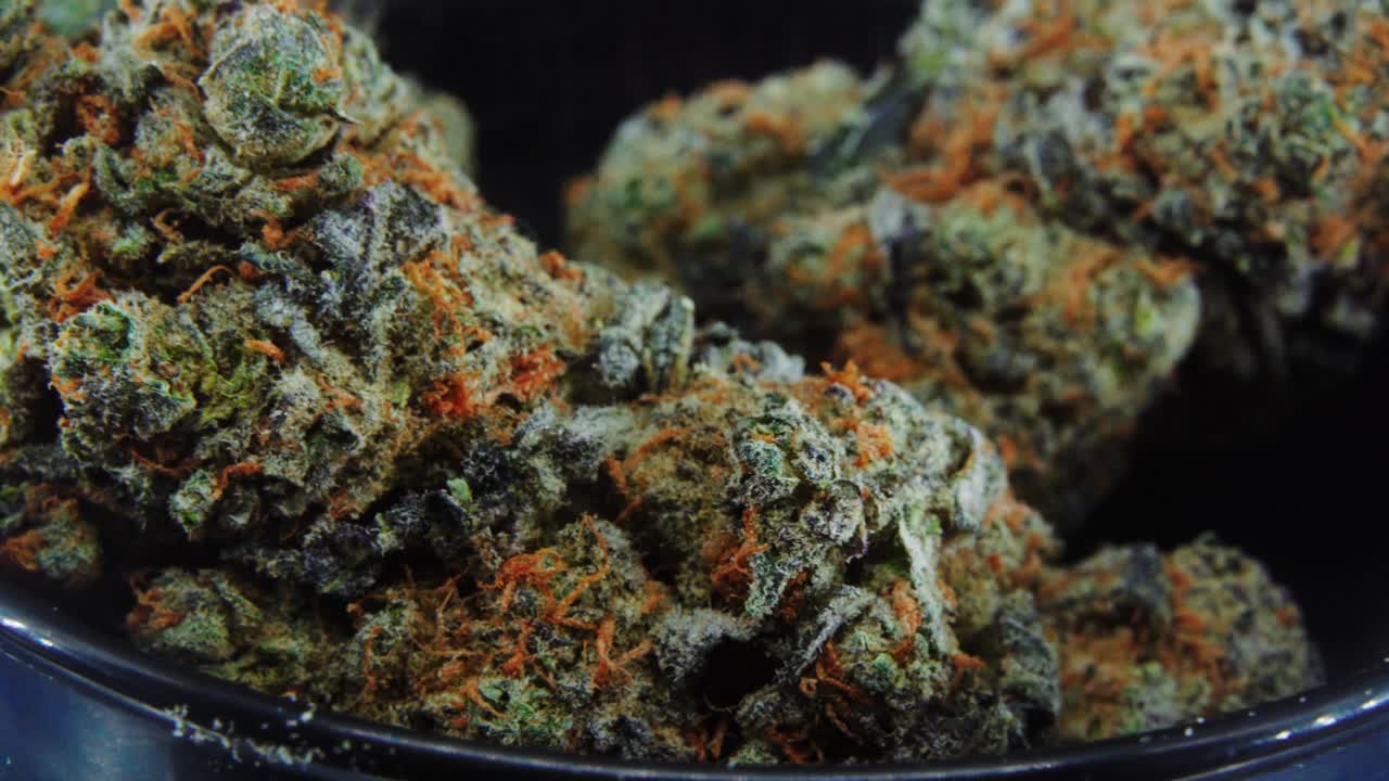 Macro Purple Green Dried Marijuana Buds Close Up concept Shot, pile of dried marijuana plants, orange trichomes strains, in small black shiny bawl, on a rotating stand, studio lights, slow motion, 4K