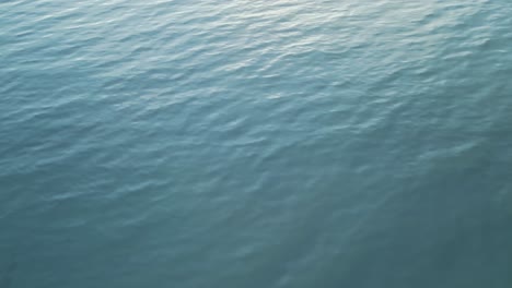 Drone-tilting-up-into-the-horizon-over-the-water-during-sunset