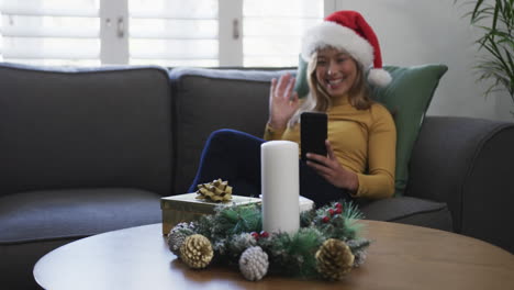 Fröhliche-Biracial-Frau-Mit-Weihnachtsmütze-Und-Smartphone-Zu-Weihnachten,-Kopierraum,-Zeitlupe