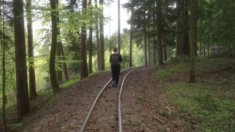 girl walks along the abandoned tracks in the forest with a backpack