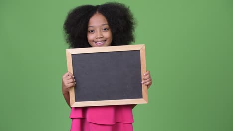 une jeune fille africaine mignonne avec des cheveux afro tenant un tableau noir.