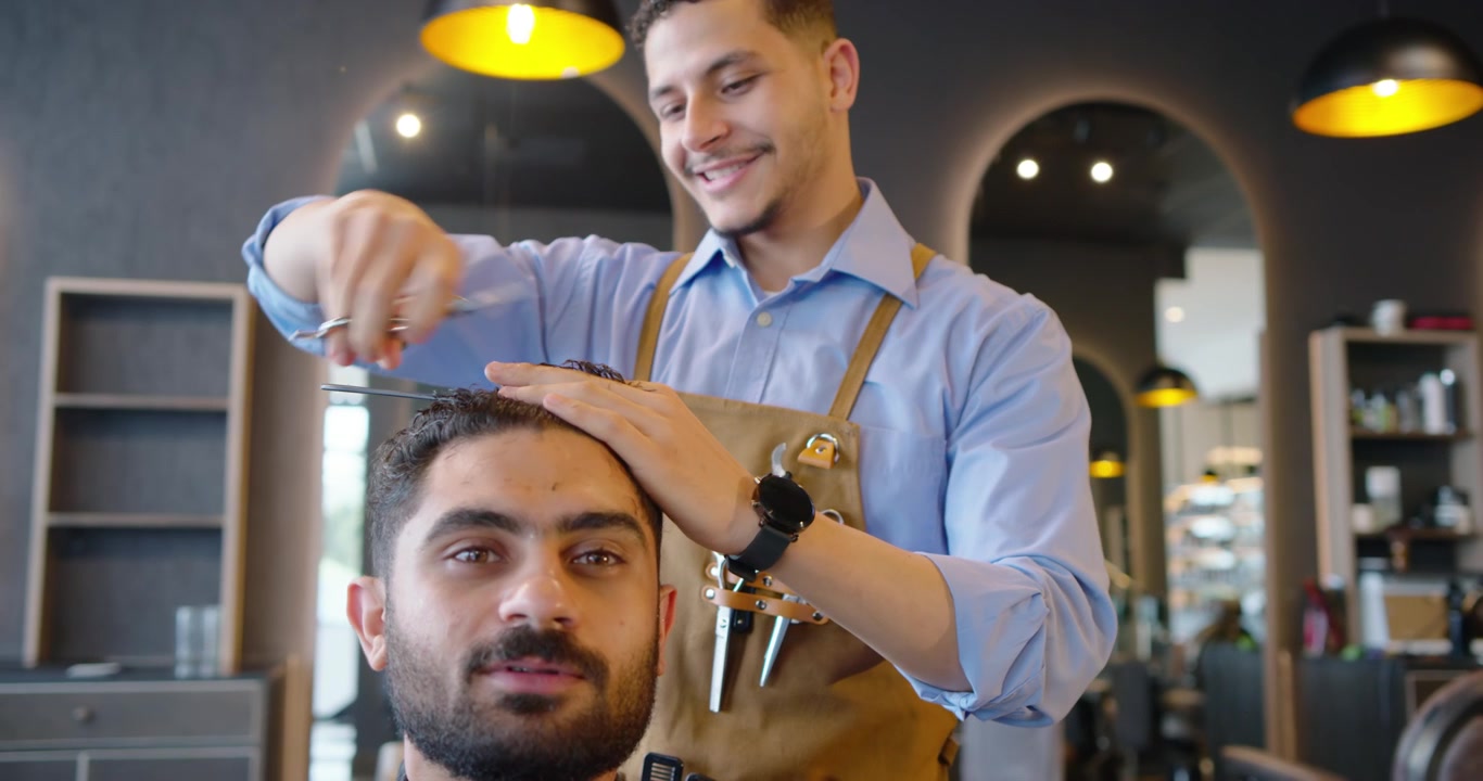 En afroamerikansk barber tjekker hår i en barbersalon, bruger kam og saks til at forme den forreste hårgrænse.