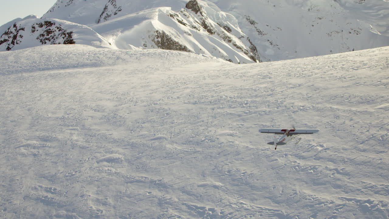воздушная съемка небольшого самолета, летящего над горой, покрытой снегом