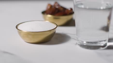 close up of bowl of dates with sugar and glass of water on marble surface celebrating muslim festival of eid