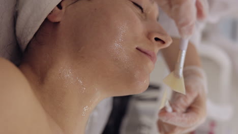 enzyme therapy beautician applying moisturizing medical cream on middleaged woman face with brushes