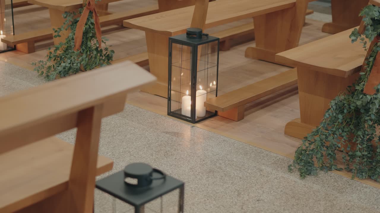 Lit candle lantern on aisle between wooden benches indoors