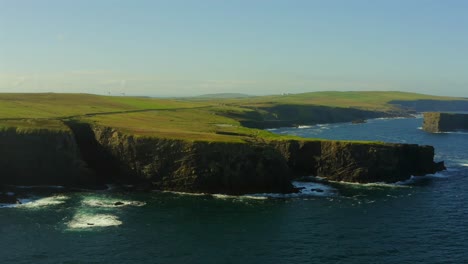 aerial dynamic shot of kilkee cliffs, featuring the main parking, cliffed promontory, and windmills in the background