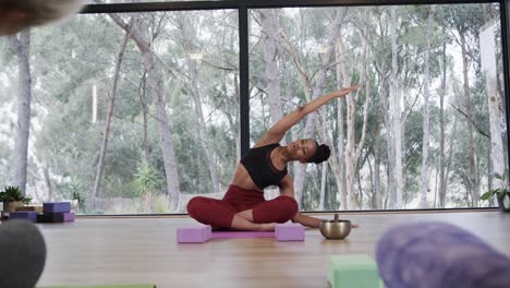 mujeres diversas estirándose juntas en esteras en la clase de yoga con una entrenadora femenina, cámara lenta