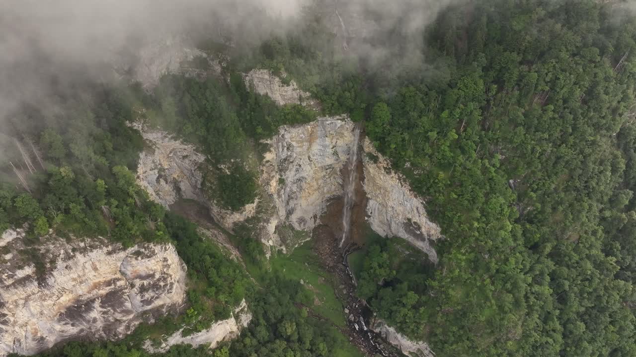 High aerial view of Seerenbach Falls plunging through cliffs into lush forest near Walensee, Switzerland, surrounded by mist and dramatic alpine scenery