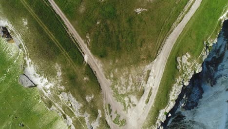 aerial view of a dirt road winding through a green valley and cliffside