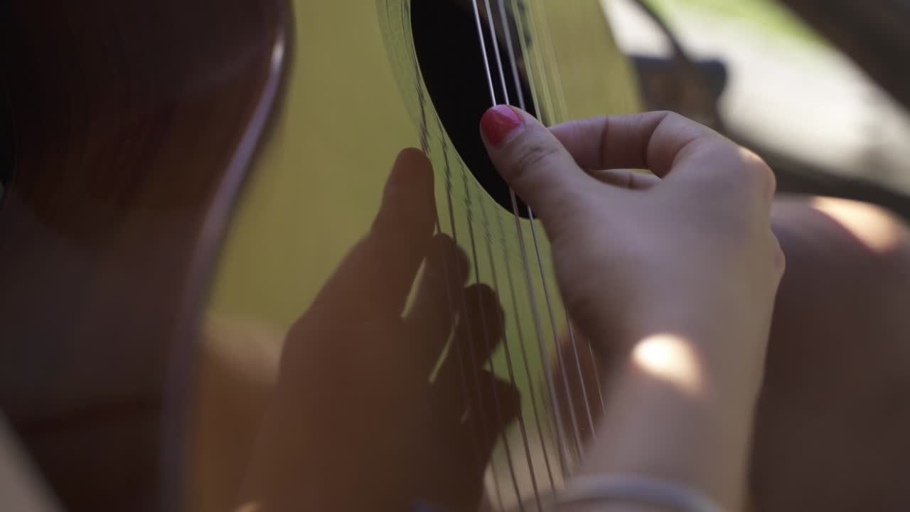 mujer joven amablemente tocando la guitarra al aire libre primer plano de la luz del día cámara lenta y 60fps