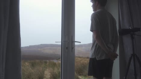 person waits and watches behind window as it is raining heavily and about to storm