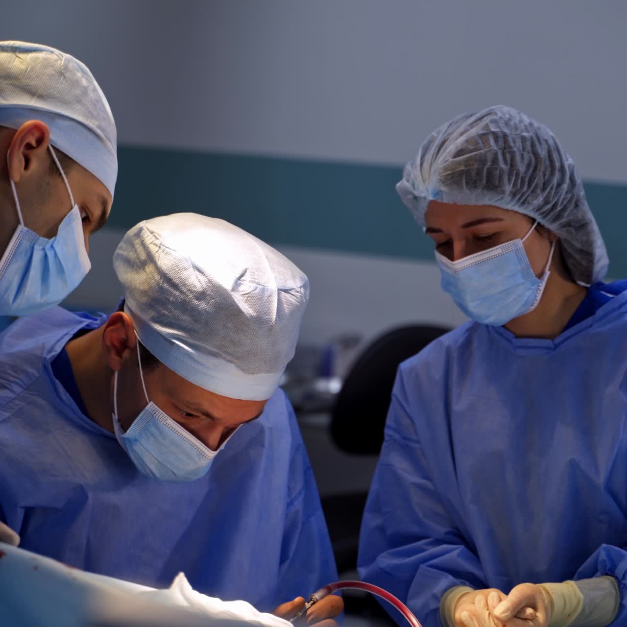 Surgeon team bent over the patient to operate him. Chief surgeon applying tools at the surgery. Assistant watching the work attentively