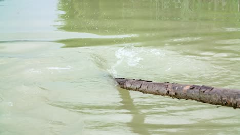 The-wooden-oar-in-muddy-river-water-of-Drava,-Slovenia-in-slow-motion