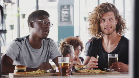 two male friends eating food and drinking beer in sports bar