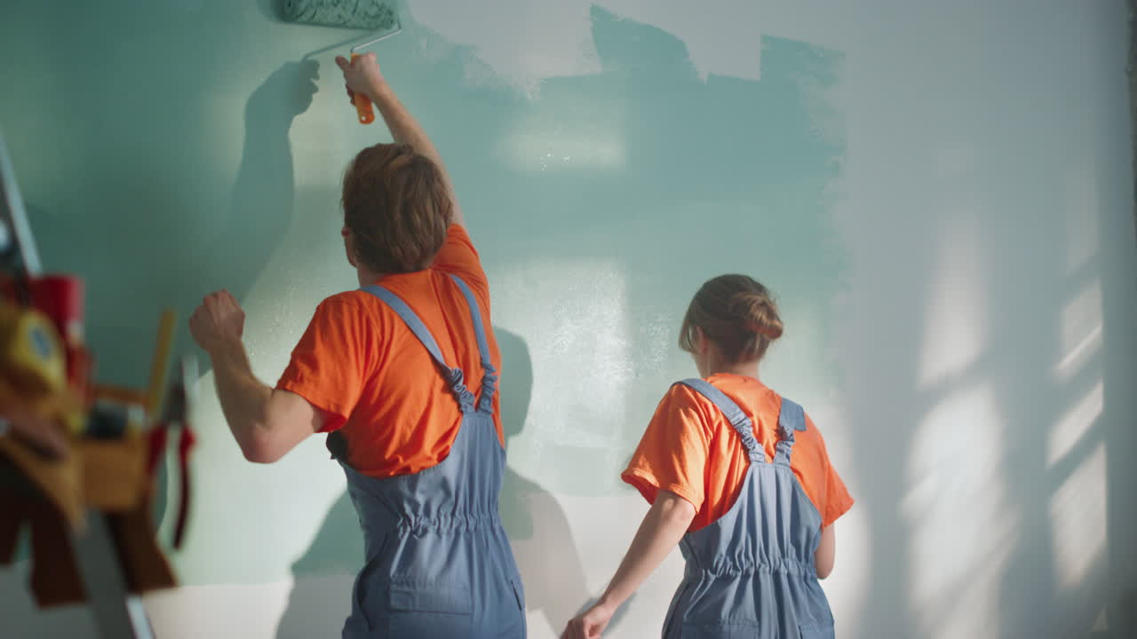 vista trasera de una pareja pintando la pared en el interior. una familia haciendo mejoras interiores.