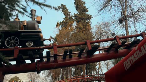 tilt down of the tren minero ride with a group of people walking under the rails at the fantasilandia amusement park, santiago, chile.