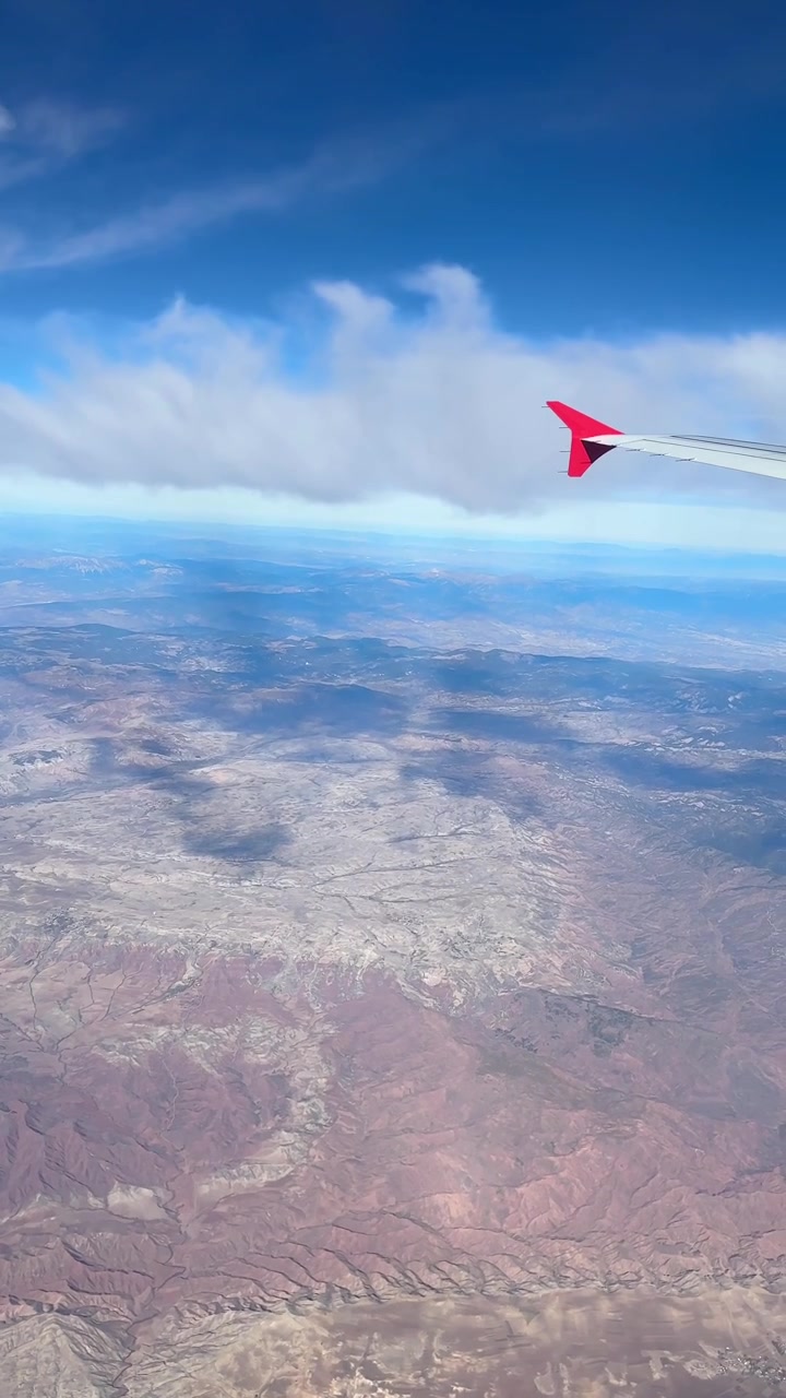 La vista dal finestrino dell'aereo rivela un vasto terreno desertico, formazioni nuvolose e l'ala dell'aereo, mostrando il viaggio aereo sopra il Marocco.